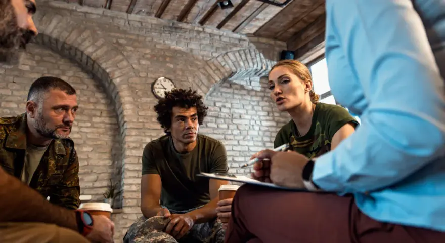Grupa żołnierzy na terapii. Kobieta w mundurze mówi, mężczyźni słuchają. Może to najbardziej luksusowe więzienie na świecie?