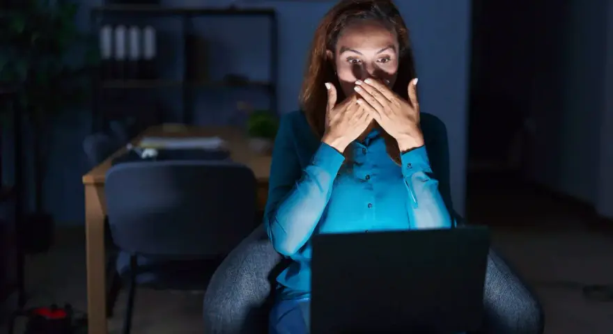 Kobieta zszokowana treścią na laptopie, czuje się jakby była obiektem prześladowania kogoś.