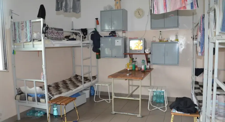 Wnętrze przypomina **zakład karny cela** z łóżkami piętrowymi, stołem, telewizorem i szafkami.