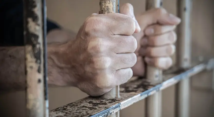 Dłonie więźnia zaciskają się na kratach. Może to być symbol nadziei na zwolnienie, gdy przygotowuje wniosek do dyrektora zakładu karnego wzór.