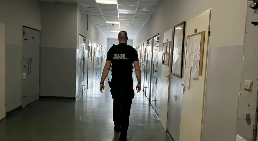 Strażnik więzienny idzie korytarzem, gdzie odbywa się klasyfikacja skazanych. Wzdłuż korytarza znajdują się cele.