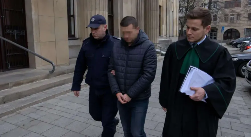 Policjant eskortuje podejrzanego przed budynkiem sądu. Ile jest więzień w Polsce? To pytanie nurtuje wielu.