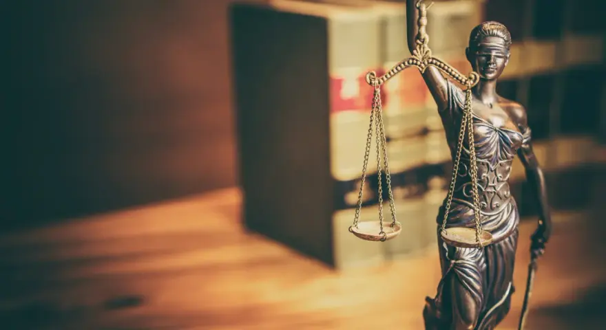 Temida z wagą i mieczem, symbol sprawiedliwości, na tle książek. Jej postawa sugeruje odrzucenie wniosku o wstrzymanie wykonania kary.