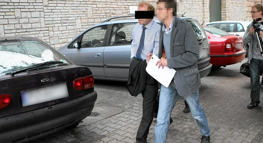 Dwóch mężczyzn, jeden w garniturze, drugi w kurtce i jeansach, idzie obok samochodów. Czy to występek, co to za sytuacja?