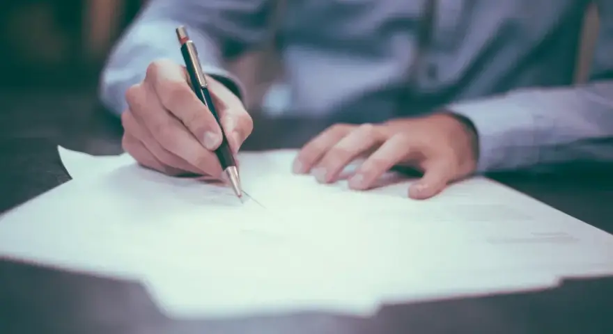Dłoń pisze długopisem na papierze. Może to być wniosek o obrońcę z urzędu.