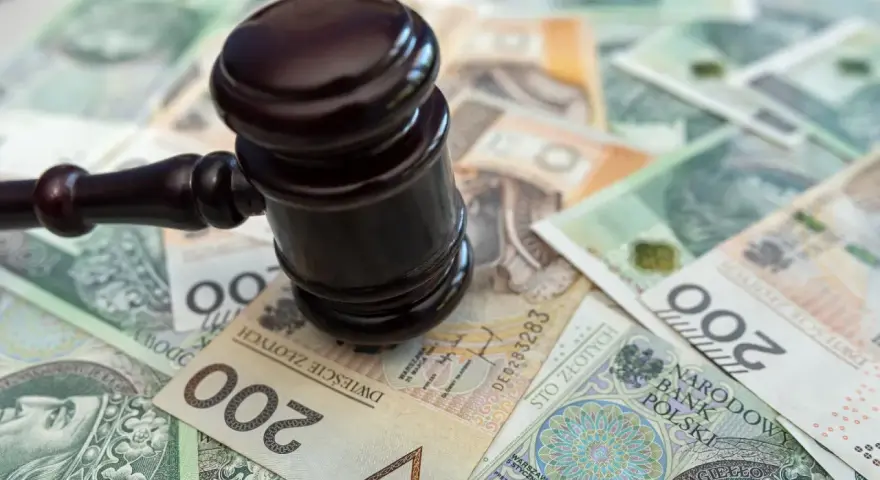 Młotek sędziowski na stosie polskich banknotów. Określenie "stawka dzienna kk" może sugerować koszty sądowe lub kary finansowe.
