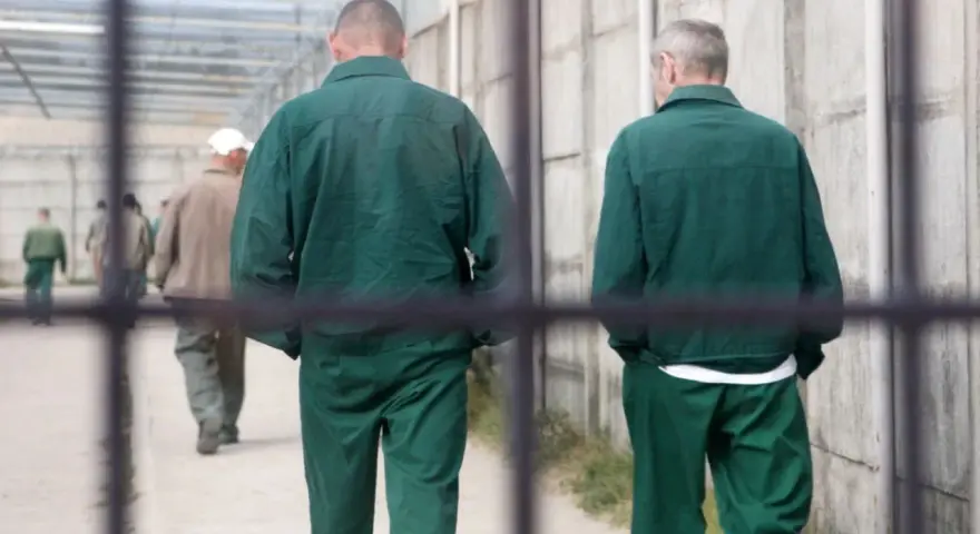 Dwóch mężczyzn w zielonych strojach więziennych w Polsce idzie korytarzem.