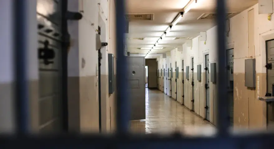 Korytarz więzienny z rzędami cel po obu stronach, widok przez kraty.