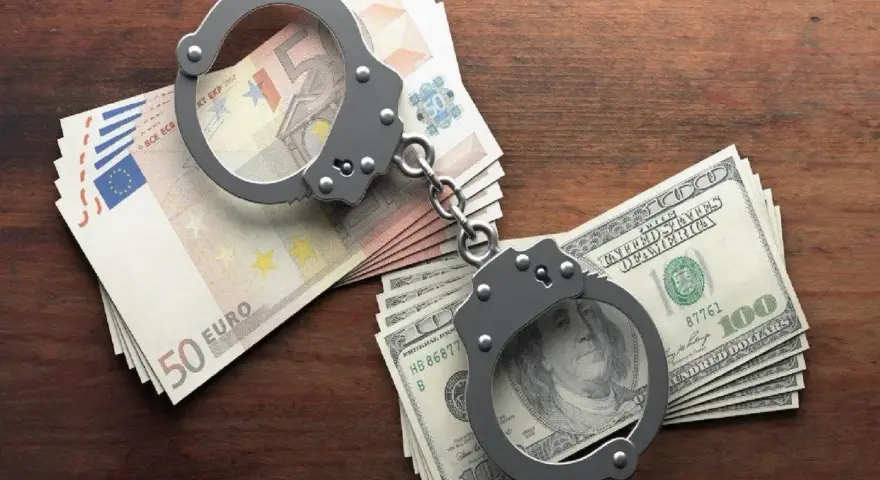 Kajdanki na stosach euro i dolarów. Symbolizują finansowe kk oszustwo i jego konsekwencje.