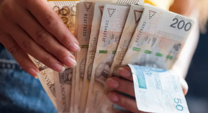 Dłonie trzymają plik banknotów 200 zł i 50 zł. Jak egzekwować obowiązek naprawienia szkody, gdy sprawca nie chce zapłacić?
