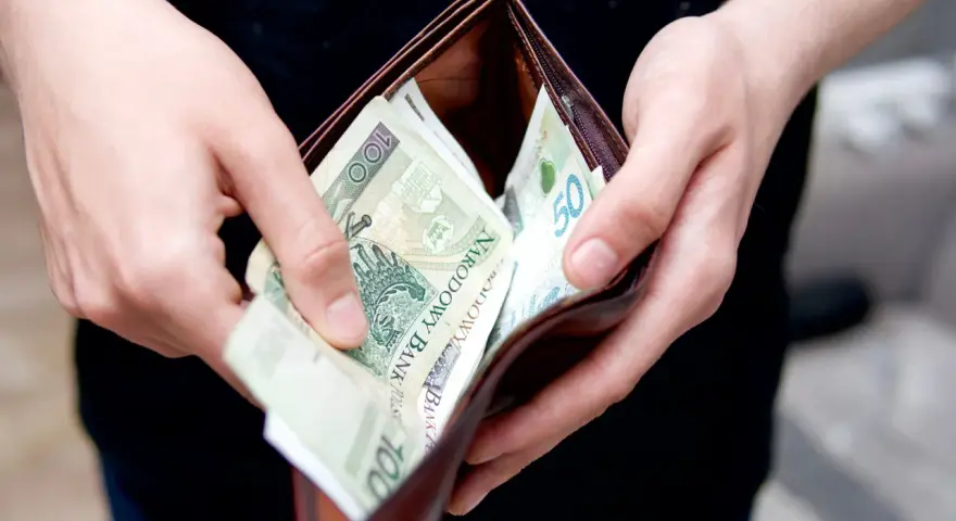 Dłonie wkładają polskie banknoty do portfela. Może to symbolizować rekompensatę za nękanie, która wreszcie trafia do poszkodowanego.