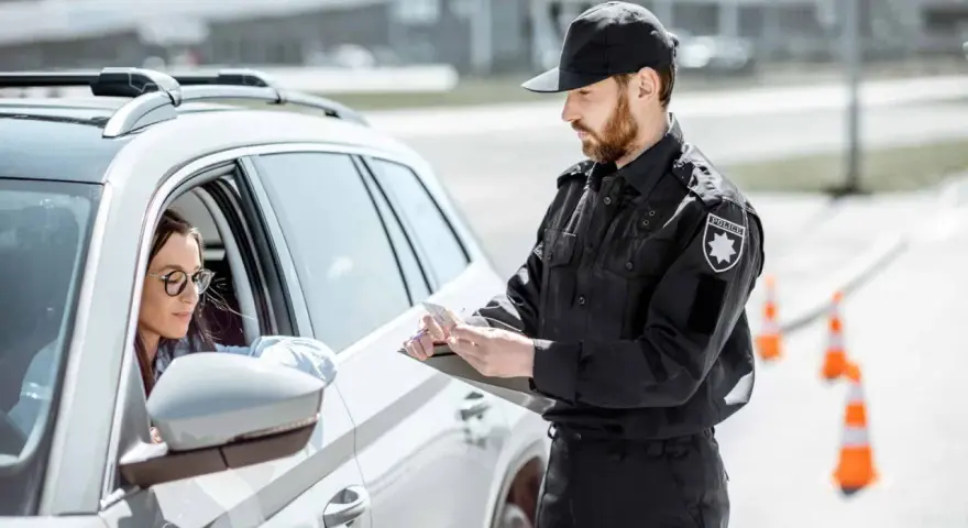 Policjant spisuje dane kierowcy, który może być zagrożony **przepadkiem pojazdu**. Kobieta w okularach siedzi za kierownicą białego samochodu.