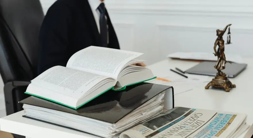 Prawnik w garniturze studiuje kodeks, art. 11 kpk, obok stosu akt i gazety "Dziennik Gazeta Prawna".