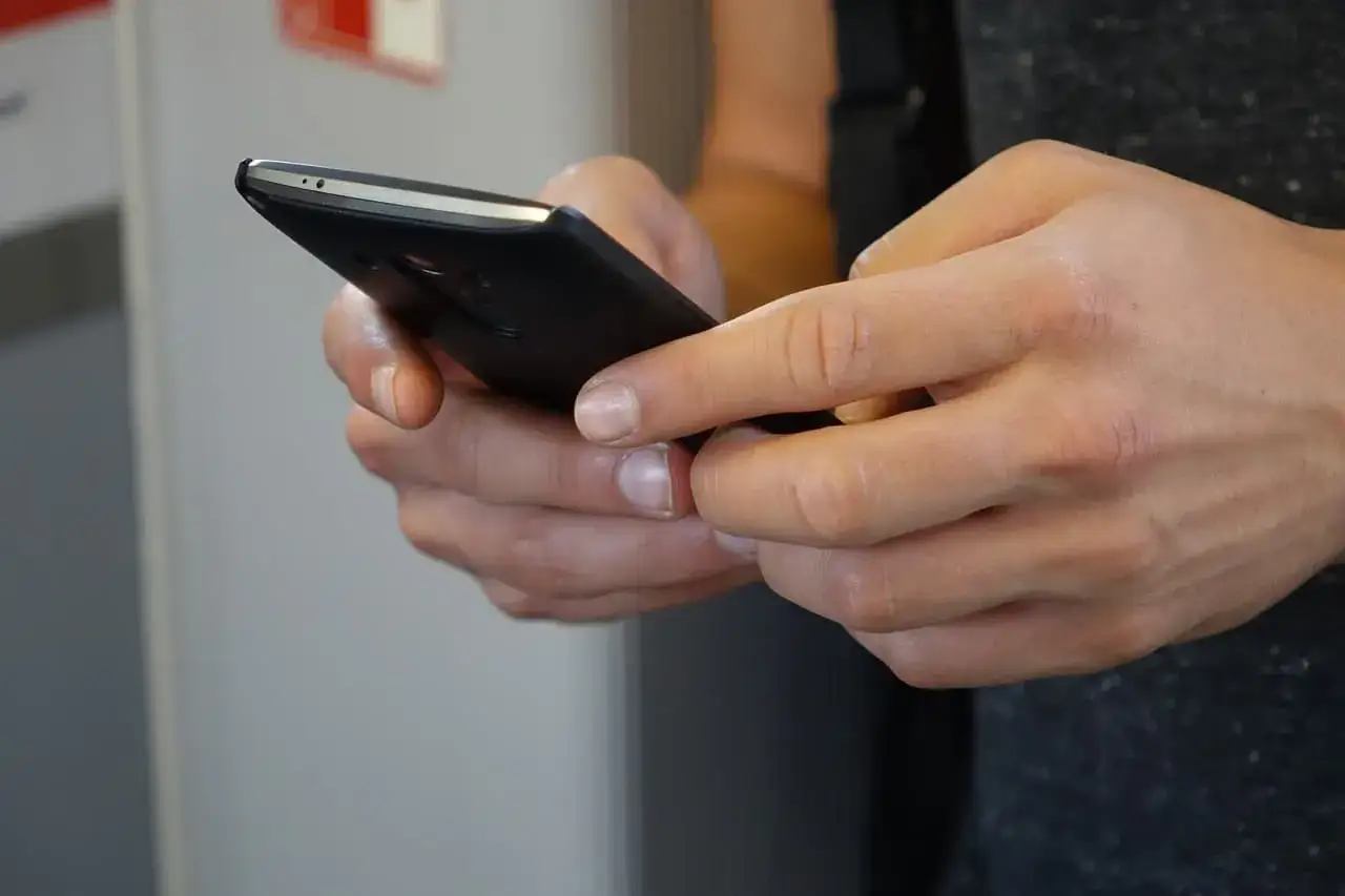 Dłonie trzymające smartfon. Uważaj, co piszesz, bo za nękanie smsami grożą konsekwencje prawne.