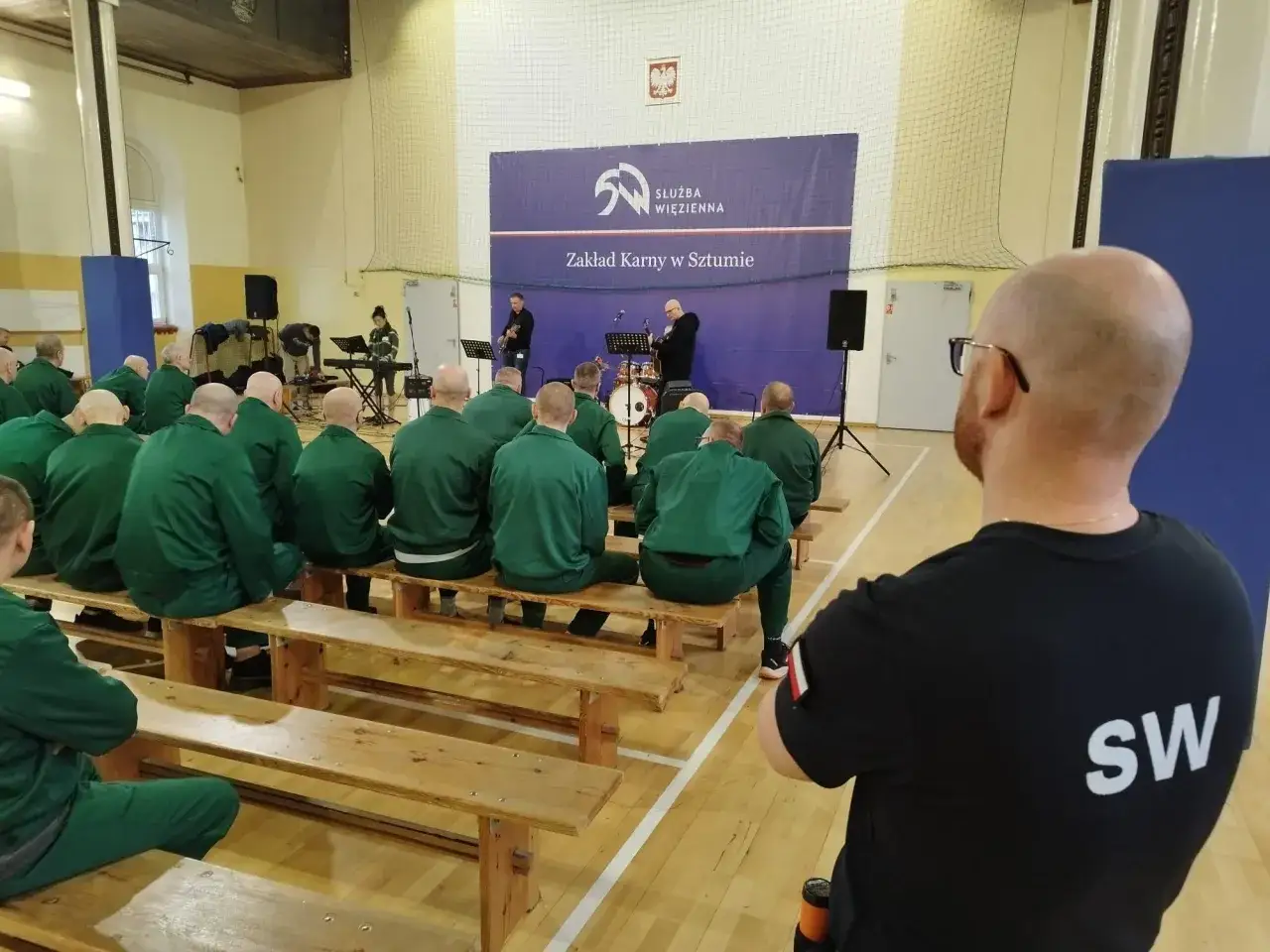 Pierwsze widzenie w zakładzie karnym w Sztumie. Muzycy grają dla osadzonych siedzących na ławkach.