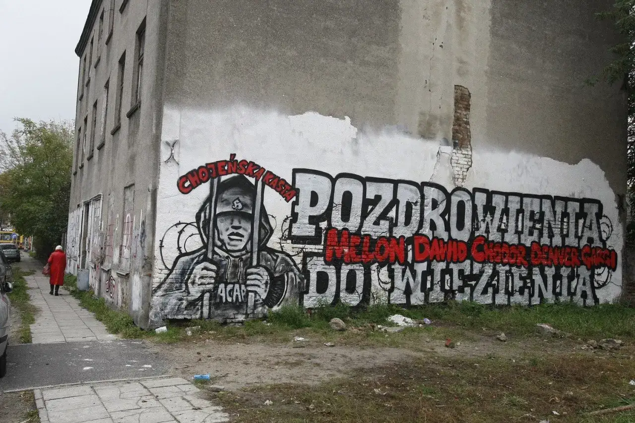 Graffiti na ścianie kamienicy: postać w kapturze za kratami, napis 