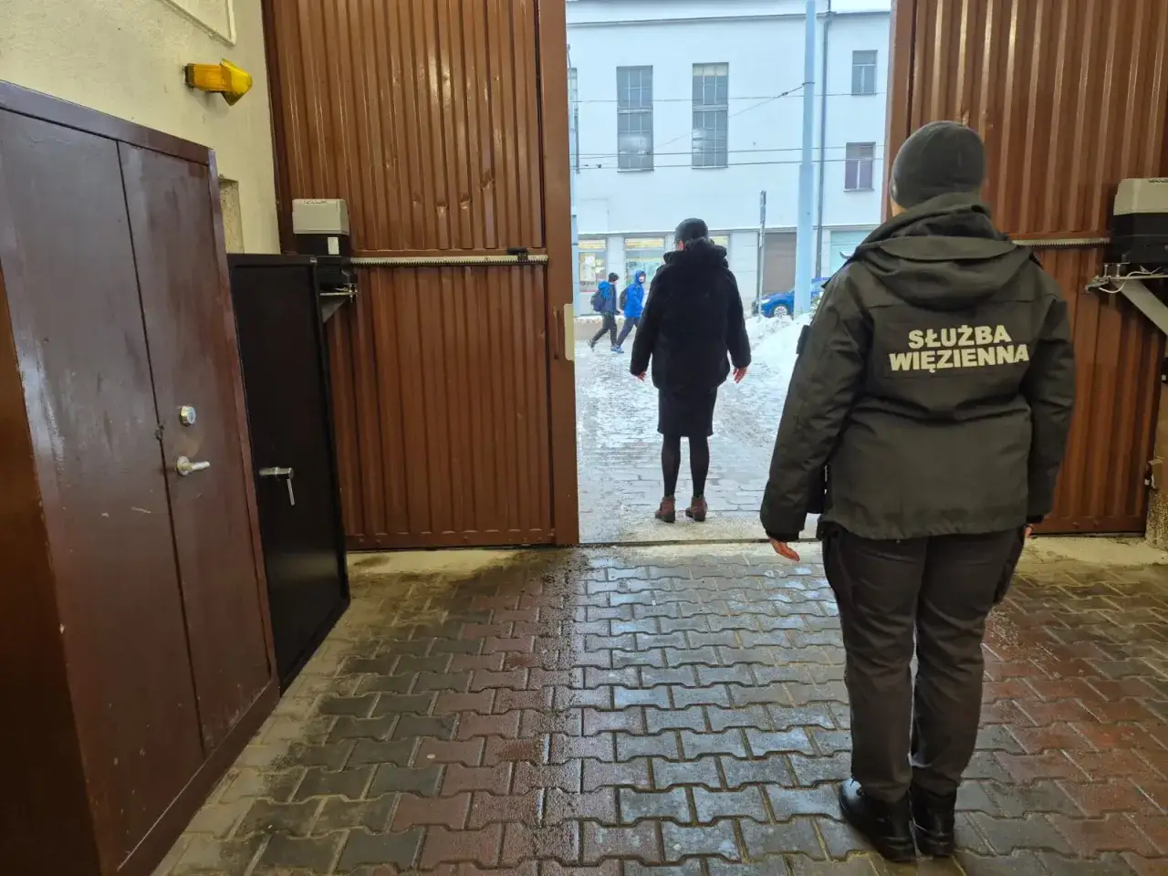 Strażniczka Służby Więziennej obserwuje osoby wychodzące na wolność, być może składające wniosek o zapomogę po wyjściu z więzienia.