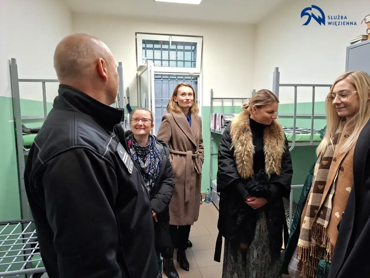 Pierwsze widzenie w zakładzie karnym. Strażnik oprowadza delegację po celi z piętrowymi łóżkami.