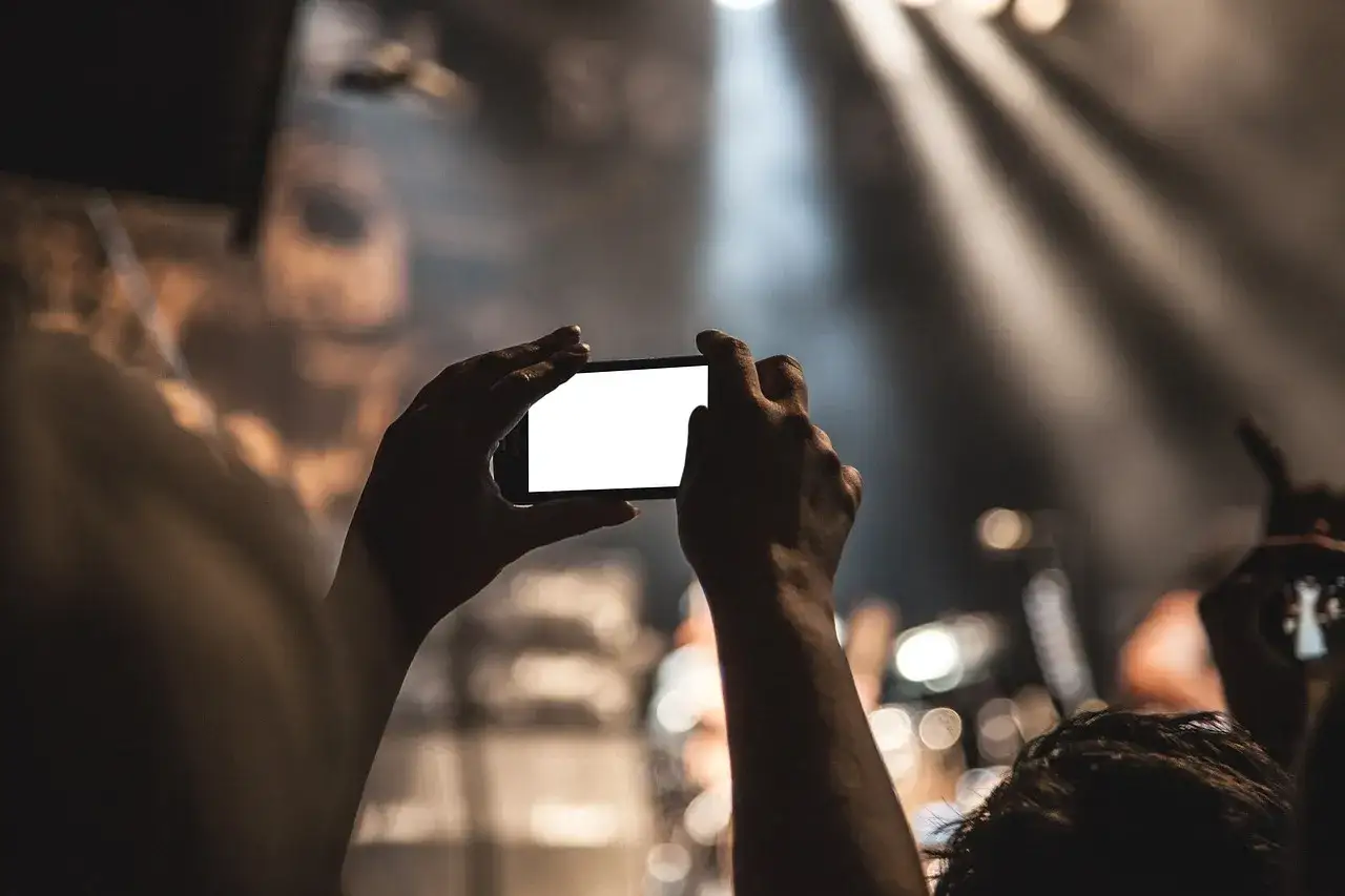 Dłonie trzymają telefon, nagrywając koncert. Czy nagranie z telefonu może być dowodem w sprawie karnej?