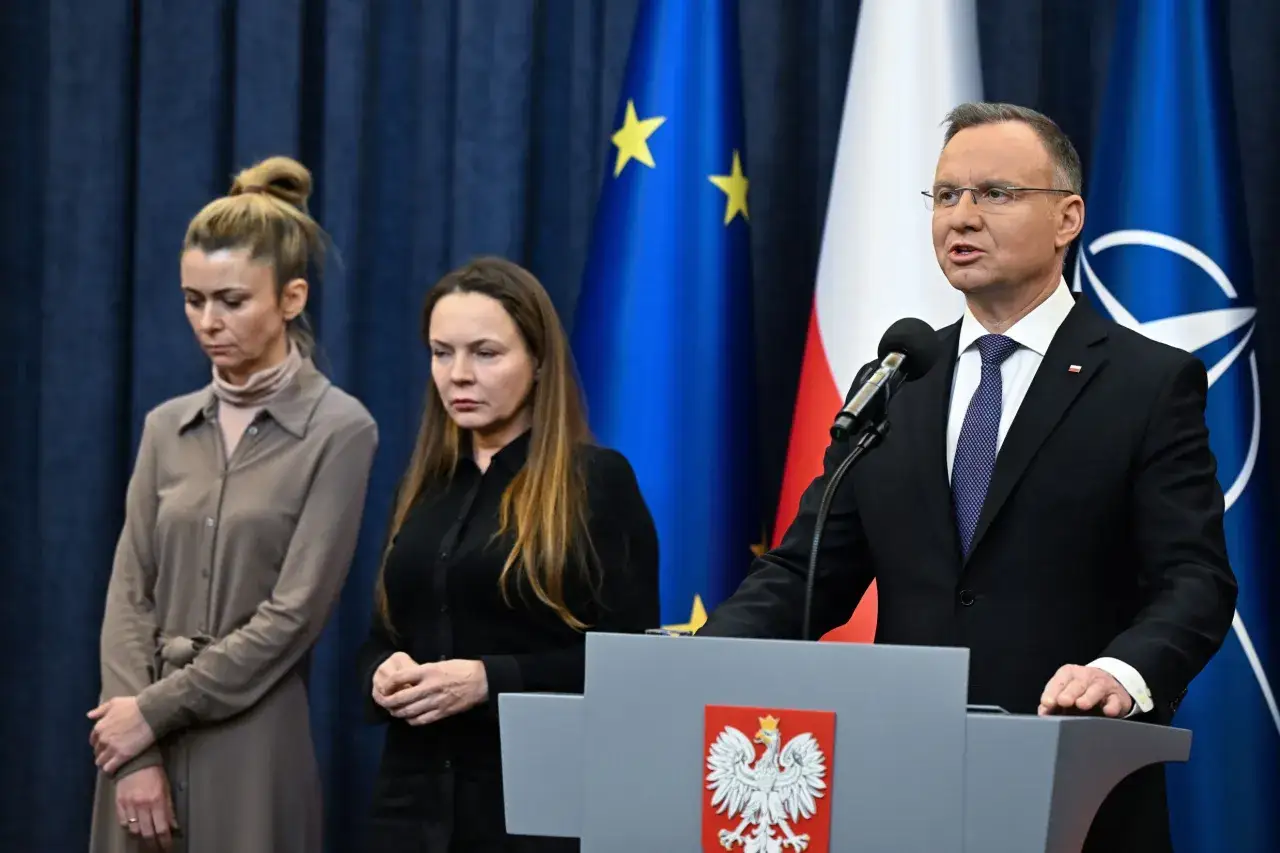 Prezydent Andrzej Duda ogłasza ułaskawienie, stojąc obok dwóch kobiet na tle flag UE i NATO.