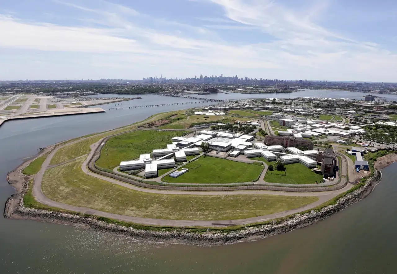 Widok z lotu ptaka na kompleks budynków więziennych na wyspie. W oddali widać panoramę miasta. To rikers island więzienie.