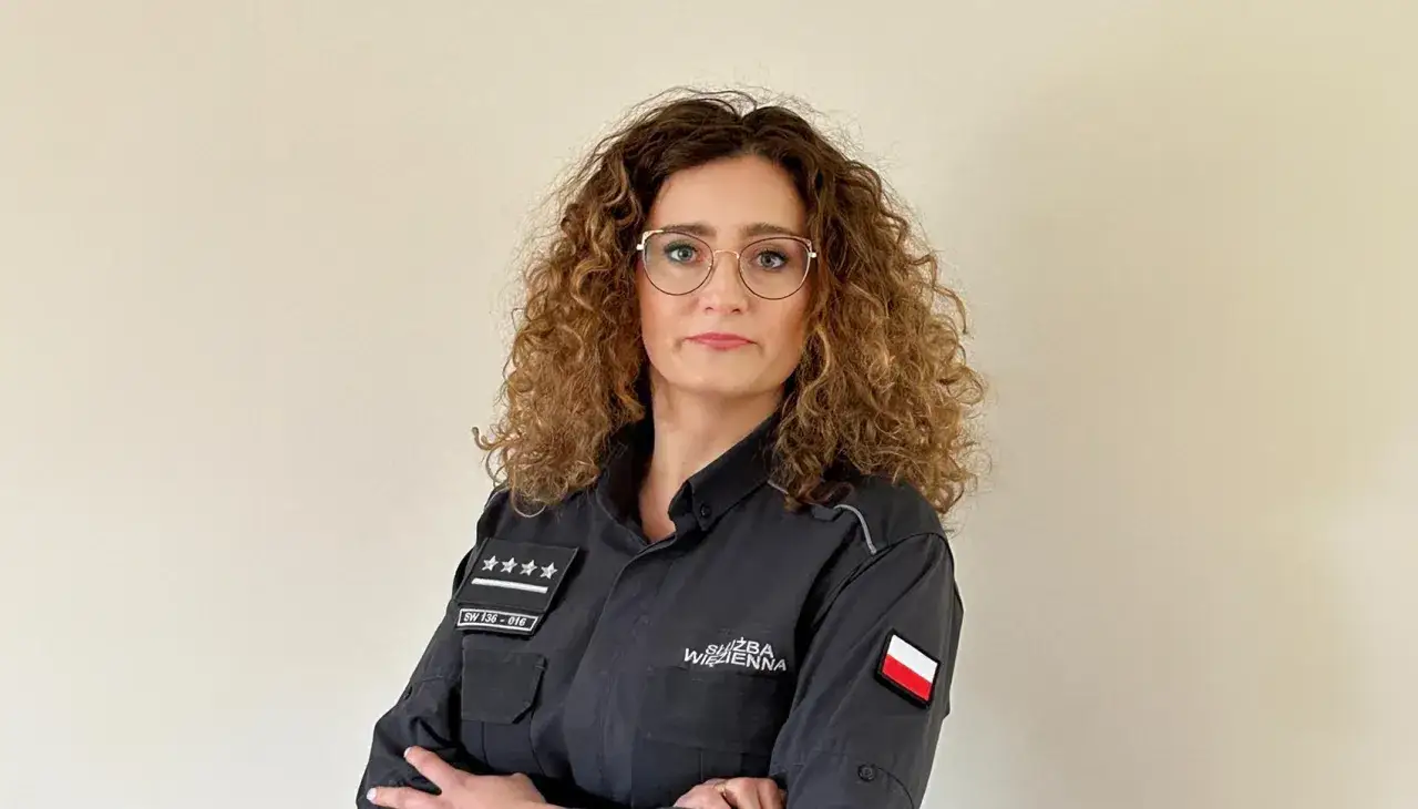 Kobieta w mundurze Służby Więziennej, pracująca w zakładzie karnym dla kobiet, z dumą prezentuje swoją odznakę.