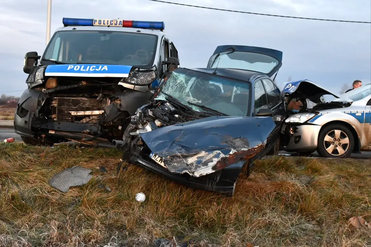 Zniszczone samochody po wypadku, w tym radiowóz. Widoczny przód ciemnego auta, maska wygięta, szyba pęknięta. Przepadek pojazdu po kolizji.