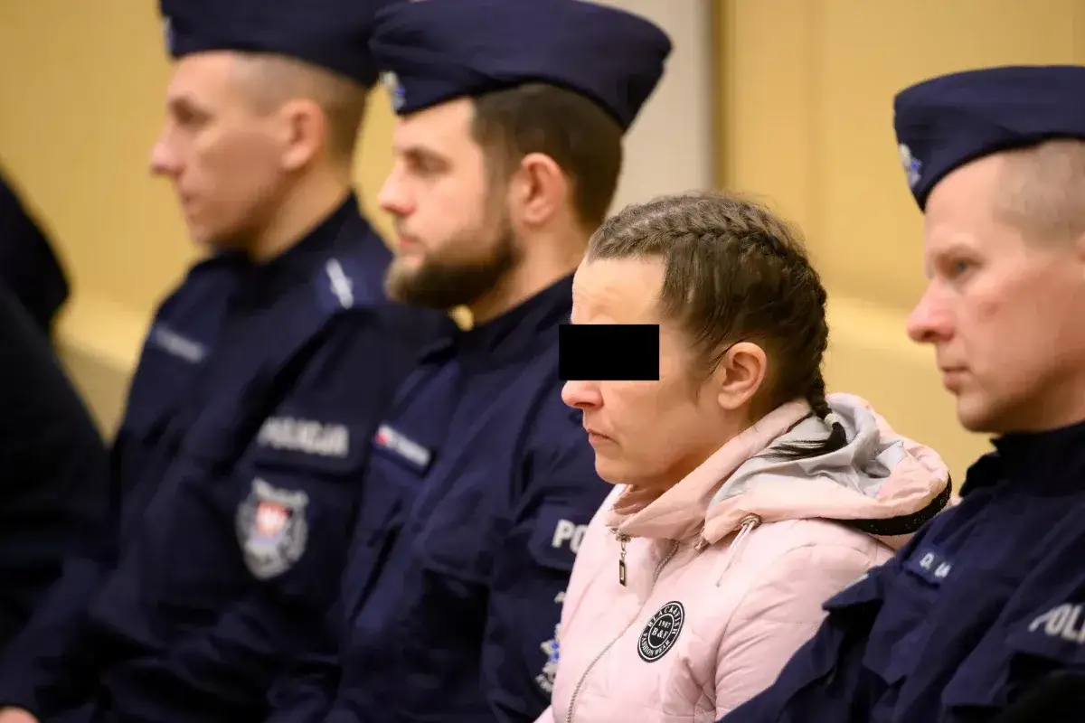 Kobieta z zakrytą twarzą siedzi w otoczeniu policjantów, oczekując na wyrok.