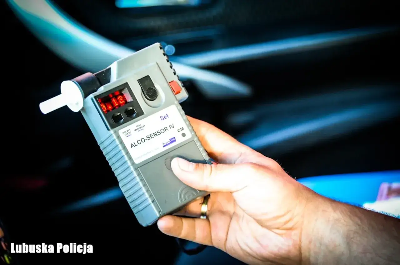 Policjant przeprowadza procedurę badania alkomatem. Na ekranie urządzenia widoczny wynik 0.12.