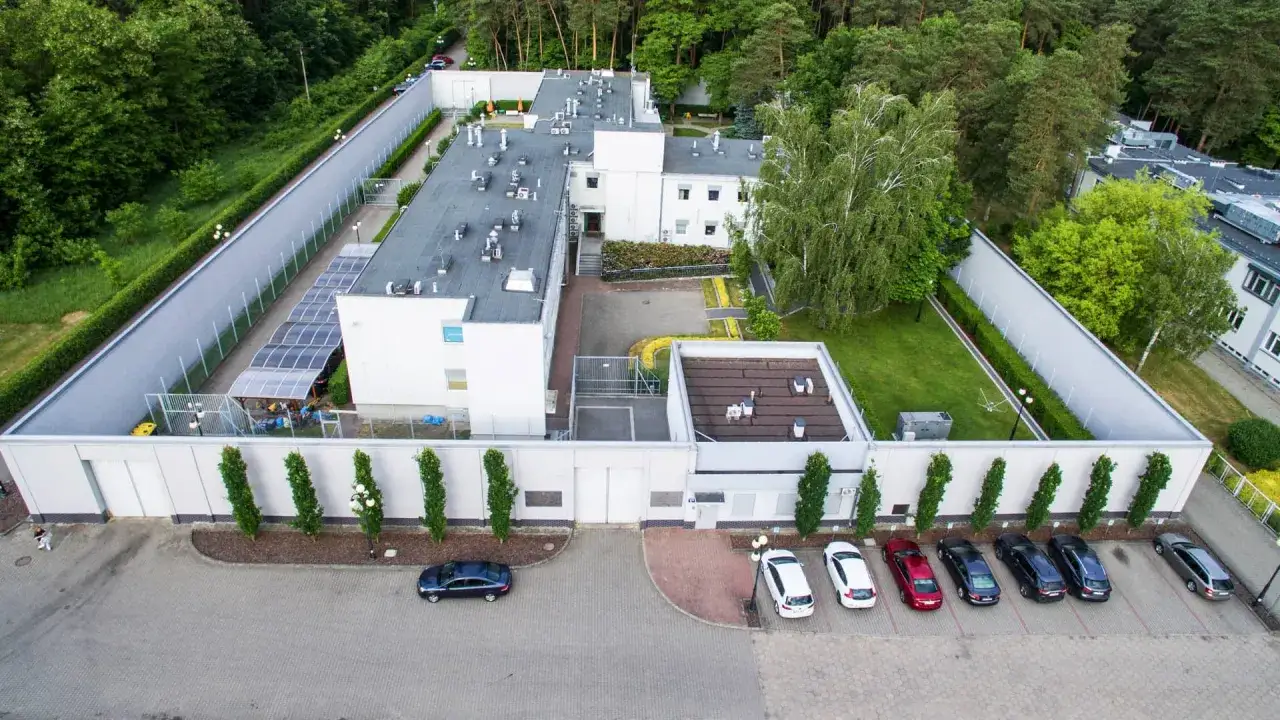 Widok z lotu ptaka na ośrodek w Gostyninie. Budynki otoczone zielenią, parking z samochodami.