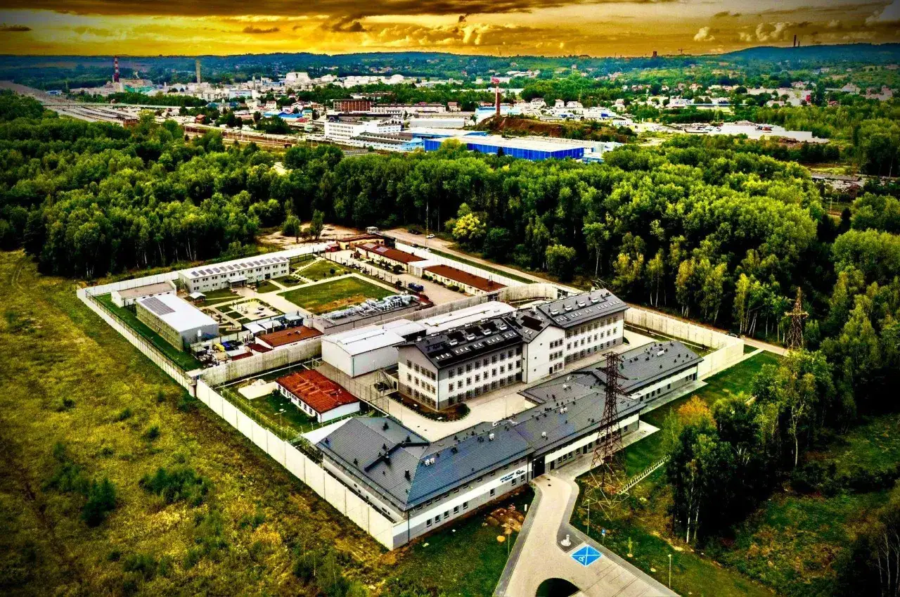 Widok z lotu ptaka na zakład karny typu otwartego w Polsce, otoczony lasem i polami.
