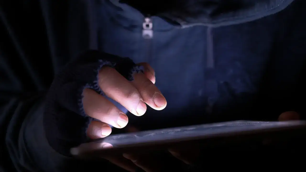 Dłoń w rękawiczce bez palców pisze na tablecie, grożenie postępowaniem karnym wisi w powietrzu.