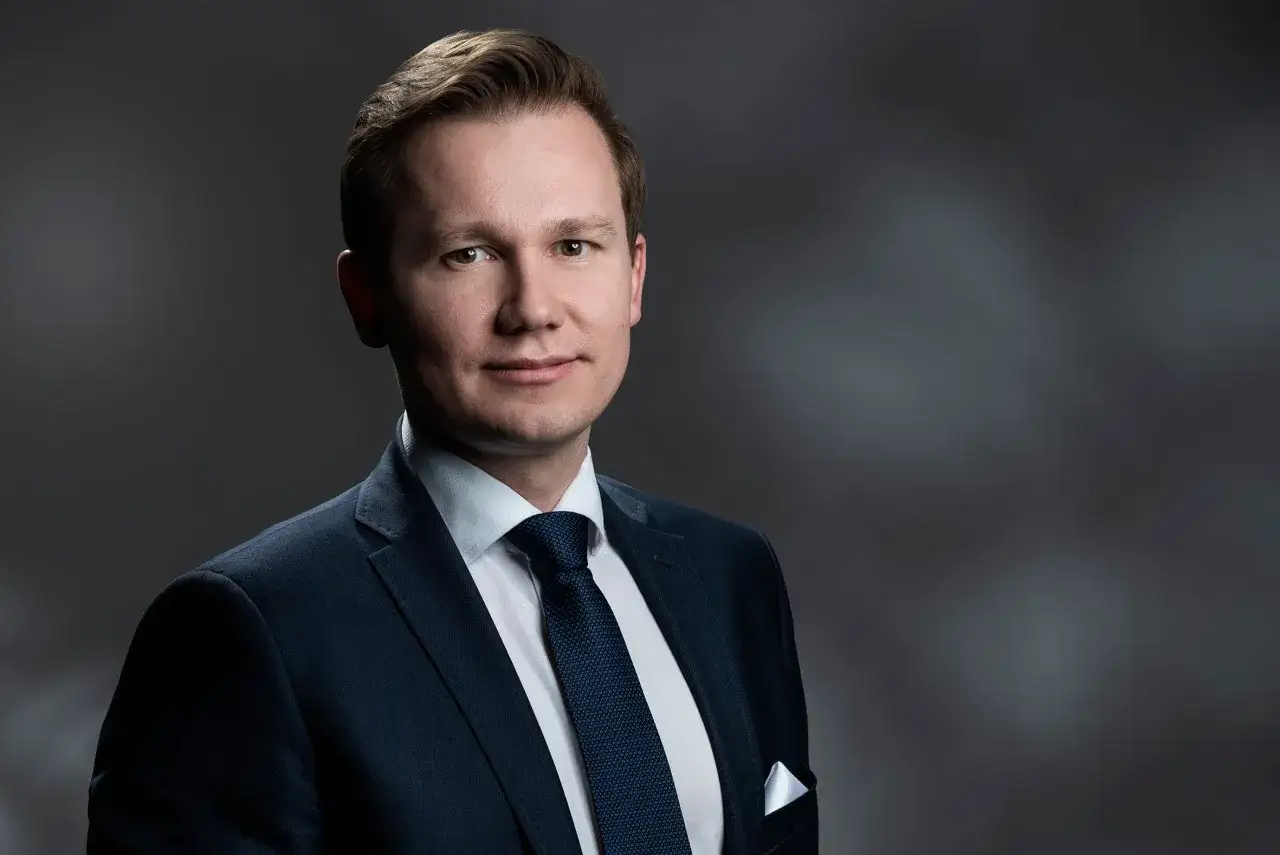 Mężczyzna w granatowym garniturze, białej koszuli i granatowym krawacie. Wygląda jak prawnik z urzędu, gotowy do podjęcia ważnych spraw.