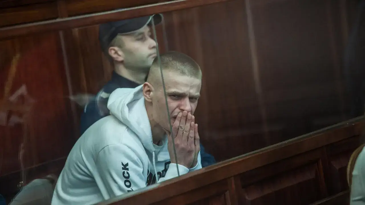 Młody mężczyzna w białej bluzie z kapturem, z dłońmi złożonymi przed twarzą, siedzi w ławie sądowej. Sprawa Tomasza Komendy budzi emocje.