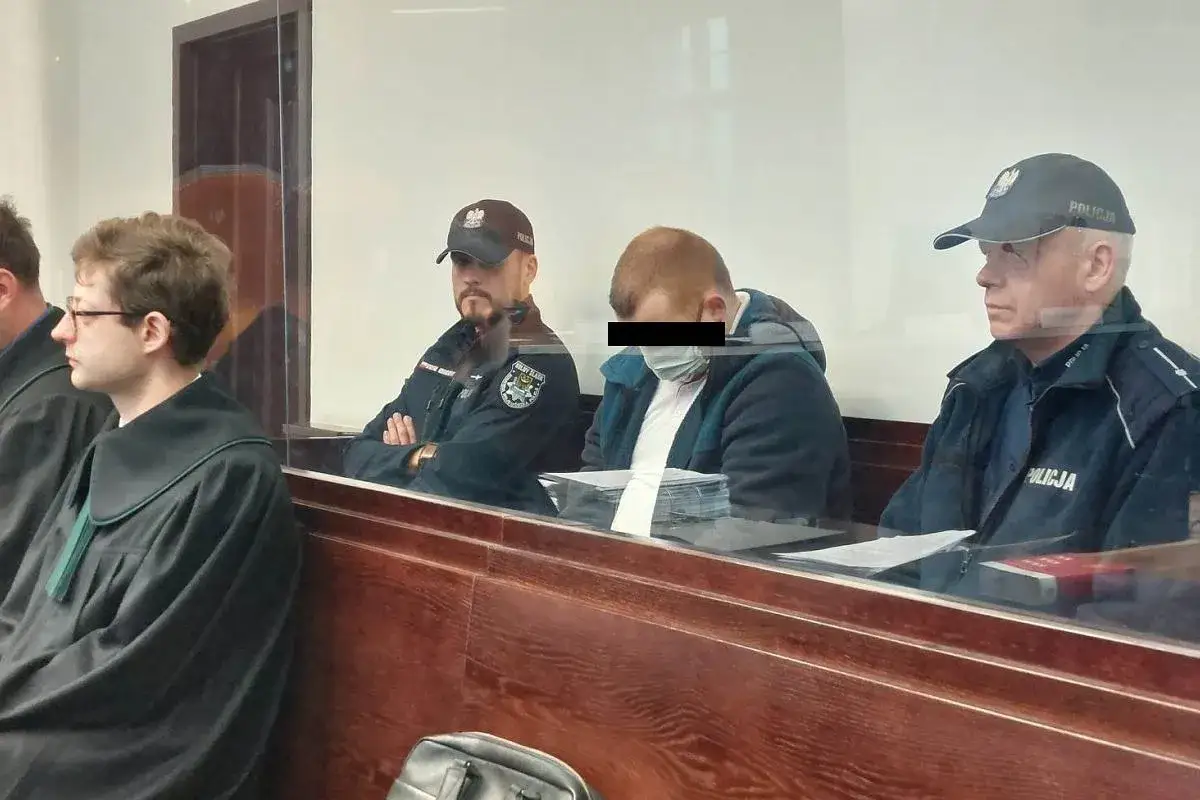 Oskarżony w masce, z zasłoniętą twarzą, siedzi między policjantami. Sąd rozpatruje sprawę, w kt&oacute;rej kluczowa jest ograniczona poczytalność.
