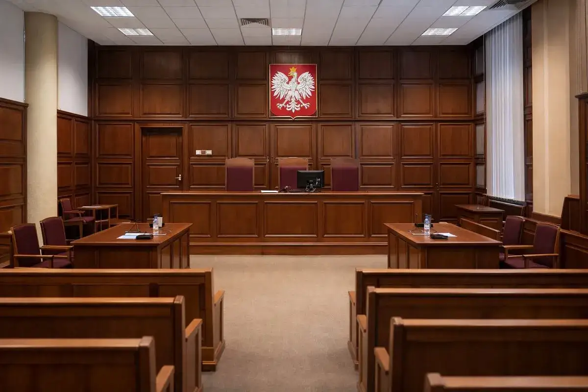 Pusta sala sądowa z orłem na ścianie. Czy poszkodowany musi być na rozprawie?