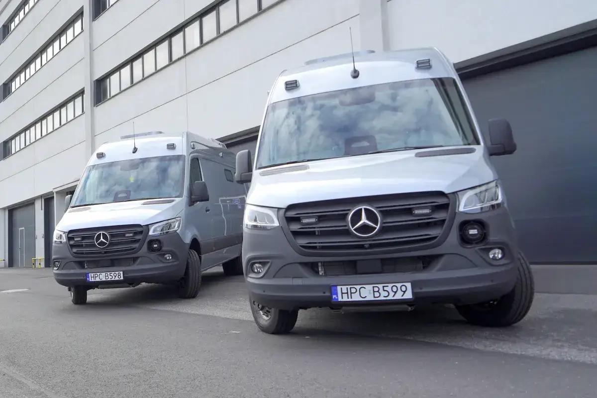 Dwie srebrne lodówki policyjne, Mercedes-Benz Sprinter, stoją przed budynkiem.