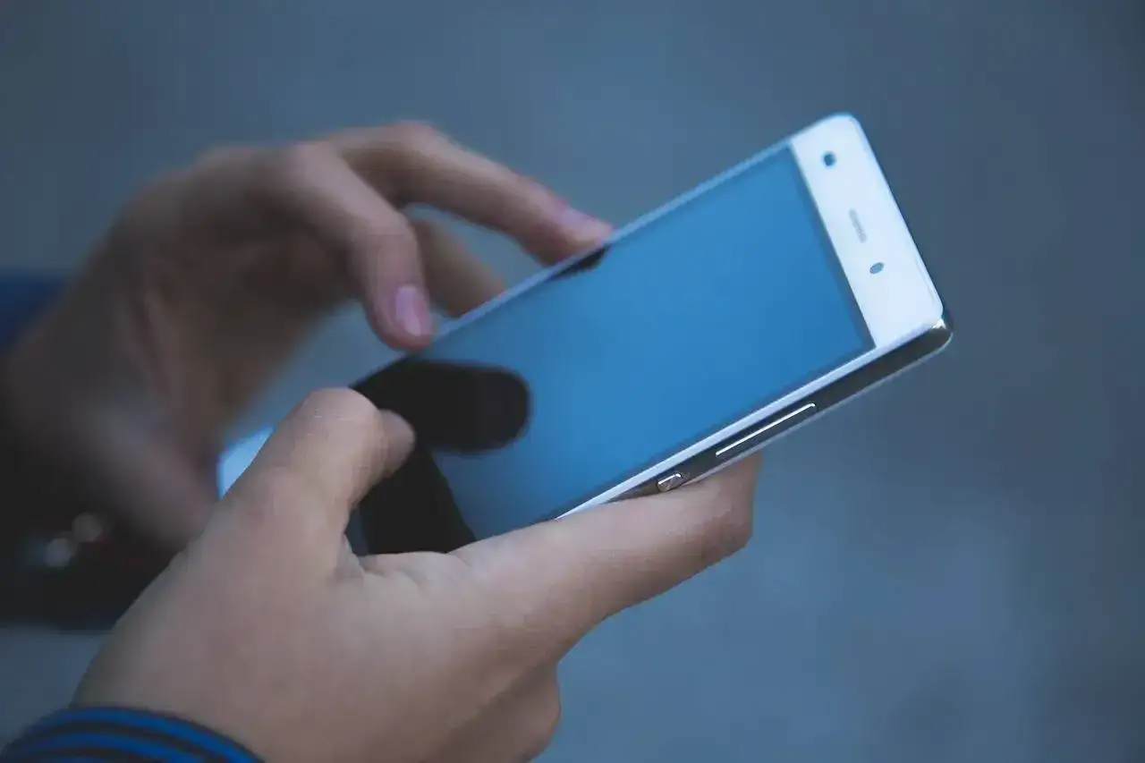 Dłonie trzymają biały smartfon. Czy na dołku można mieć telefon? Tak, jeśli jest to telefon kom&oacute;rkowy.