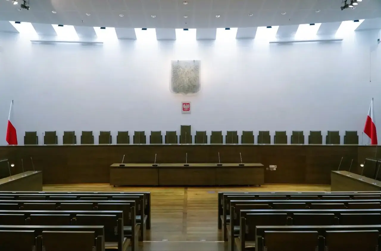 Pusta sala sądowa, gotowa na ogłoszenie wyroku w sprawie karnej. Orzeł i flagi Polski symbolizują sprawiedliwość.