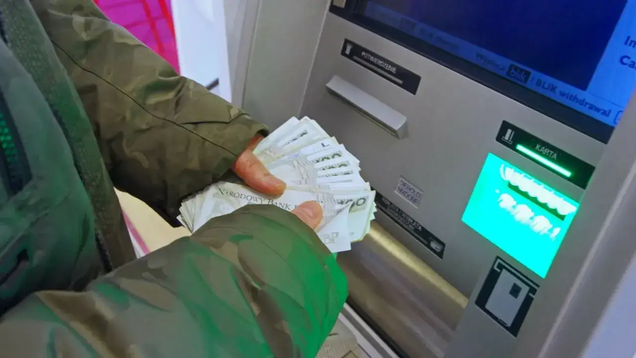 Osoba trzyma plik banknotów przy bankomacie, przygotowując się do wpłaty. To może być sposób, jak wysłać pieniądze do zakładu karnego.