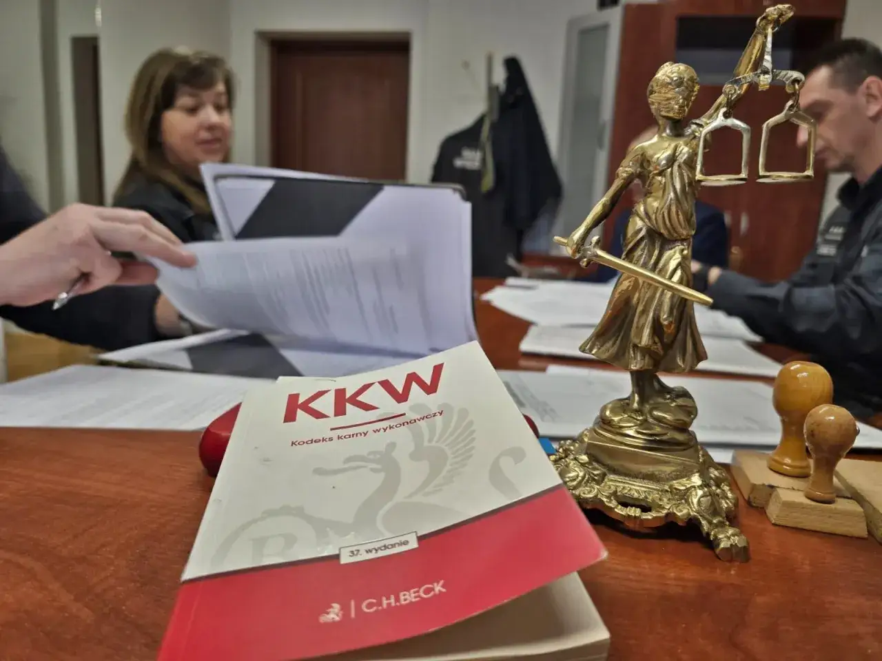 Statuetka Temidy, książka "Kodeks karny wykonawczy" i dokumenty na biurku.