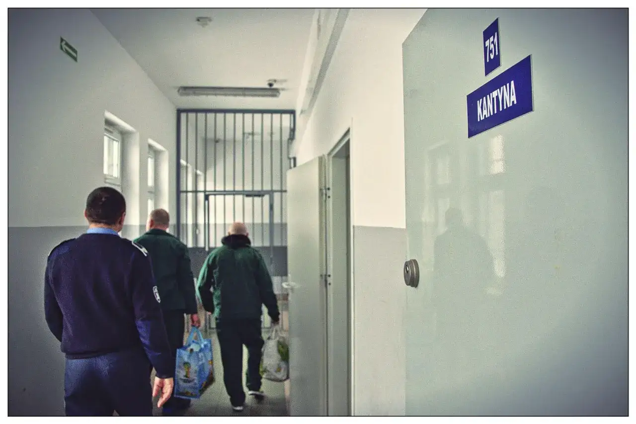 Więźniowie wracają z zakupów w więziennej kantynie, niosąc torby z zaopatrzeniem.