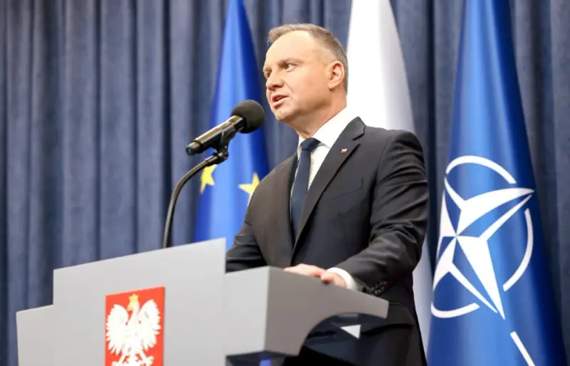 Prezydent Andrzej Duda przemawia przy mównicy z godłem Polski. Za nim flagi UE i NATO. Może to być związane z ułaskawieniem prezydenta.